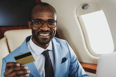 Lächelnder männlicher Unternehmer mit Kreditkarte im Flugzeug - OIPF00269