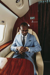 Male entrepreneur checking time on wristwatch while traveling in private jet - OIPF00282