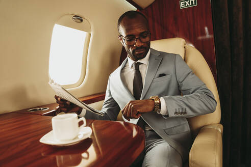 Geschäftsmann hält eine Zeitung in der Hand, während er im Flugzeug die Zeit auf seiner Armbanduhr überprüft - OIPF00283