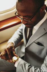Männlicher Unternehmer, der im Privatjet die Zeit auf seiner Armbanduhr überprüft - OIPF00285