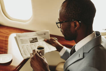 Geschäftsmann liest Zeitung während einer Reise im Flugzeug - OIPF00286