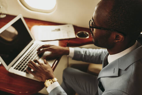 Männlicher Unternehmer, der im Flugzeug auf einem Laptop tippt - OIPF00288