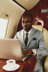 Junger männlicher Unternehmer arbeitet an einem Laptop, während er in einem Privatjet reist - OIPF00289