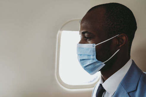 Männlicher Unternehmer mit Gesichtsschutzmaske im Flugzeug - OIPF00292