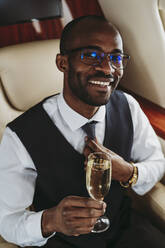 Männlicher Unternehmer mit Champagner, der eine Krawatte hält, während er im Flugzeug reist - OIPF00312