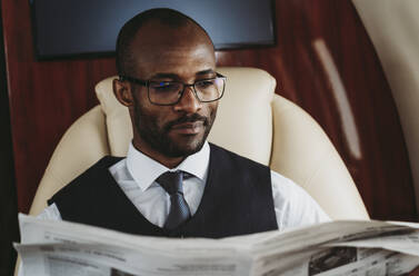 Junger Geschäftsmann liest Zeitung im Privatjet - OIPF00314
