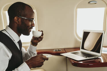 Geschäftsmann trinkt Kaffee, während er im Flugzeug am Laptop arbeitet - OIPF00321