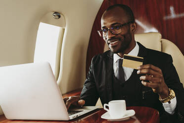 Lächelnder Geschäftsmann mit Krediten beim Online-Shopping mit Laptop im Flugzeug - OIPF00328