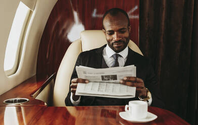 Junger Geschäftsmann liest Zeitung während einer Reise im Flugzeug - OIPF00335