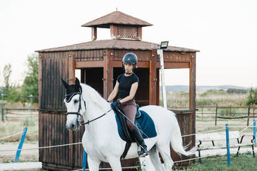 Mittlere erwachsene Frau reitet auf weißem Pferd auf einem Bauernhof - MRRF00849