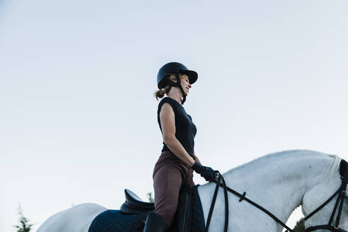 Frau mit Kopfbedeckung reitet auf Pferd gegen klaren Himmel - MRRF00850