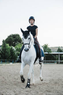 Woman wearing headwear riding white horse against clear sky in farm - MRRF00852