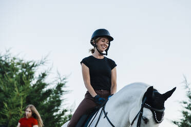 Lächelnde Frau betrachtet ihr Pferd beim Reiten am Wochenende - MRRF00854