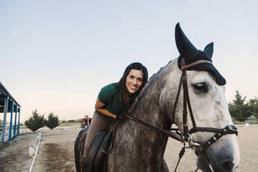 Smiling woman sitting on horse against clear sky at farm - MRRF00855