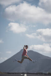 Happy male tourist jumping over highway road at Lanzarote, Spain - SNF01080