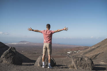 Young male tourist with arms outstretched at Femes Viewpoint, Lanzarote, Spain - SNF01085