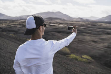 Male tourist in hat taking selfie at El Cuervo Volcano during vacations, Lanzarote, Spain - SNF01092