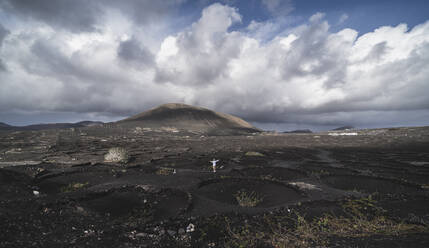 Männlicher Tourist mit ausgestreckten Armen steht auf schwarzer Vulkanasche am Vulkan El Cuervo, Lanzarote, Spanien - SNF01103