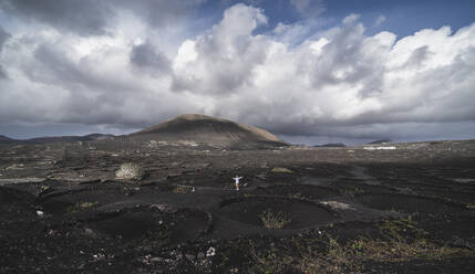 Male tourist with arms outstretched standing on black volcano ash at El Cuervo Volcano, Lanzarote, Spain - SNF01103