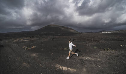 Happy male tourist dancing on volcano ash at El Cuervo Volcano, Lanzarote, Spain - SNF01105