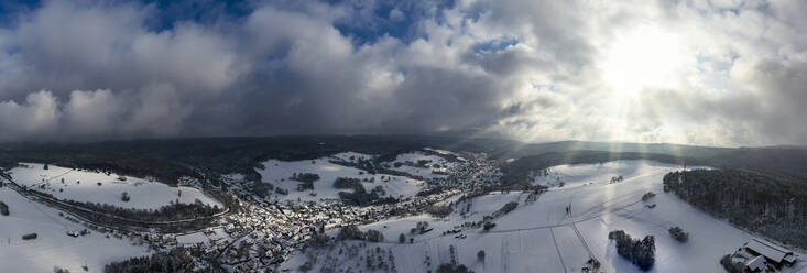 Germany, Bavaria, Mespelbrunn, Helicopter panorama of sun illuminating snow-covered town in Spessart range - AMF09037