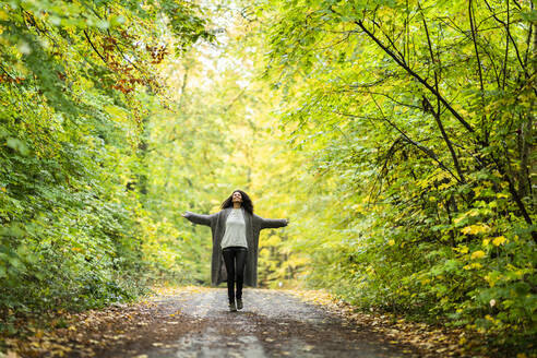 Unbekümmerte Frau mit ausgestreckten Armen, die auf einem Fußweg im Wald läuft - AKLF00001