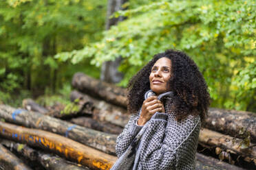 Thoughtful woman looking up while sitting in forest - AKLF00007