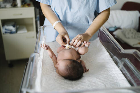 Mutter im Krankenhauskittel wechselt im Stehen die Windel ihres Neugeborenen - MPPF01480