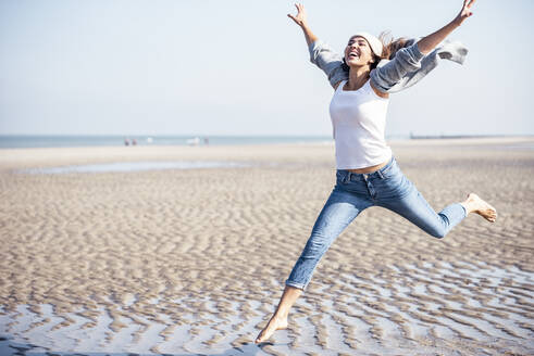 Carefree woman jumping on beach at sunny day - UUF22683
