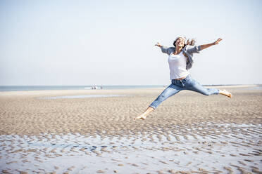 Happy young woman jumping over sand at beach - UUF22684