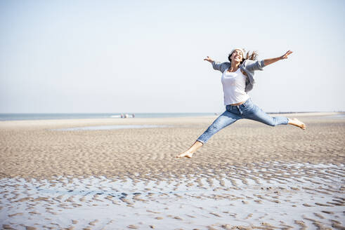 Glückliche junge Frau, die am Strand über Sand springt - UUF22684