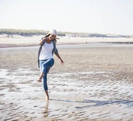 Cheerful young woman splashing water while walking on beach - UUF22687