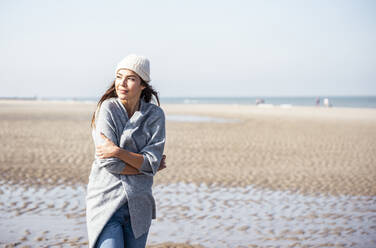 Young woman in cardigan sweater contemplating while walking on beach - UUF22688