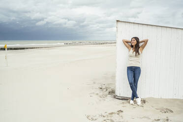 Young woman with hands behind head against beach hut during weekend - UUF22698