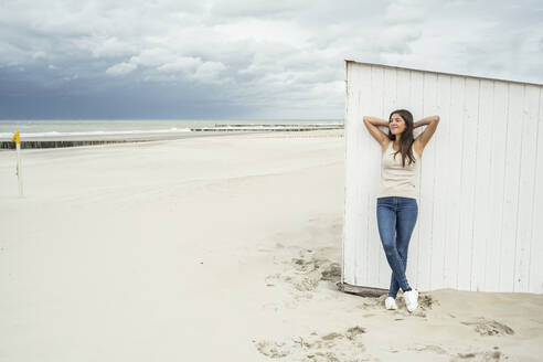 Junge Frau mit Händen hinter dem Kopf gegen Strandhütte am Wochenende - UUF22698