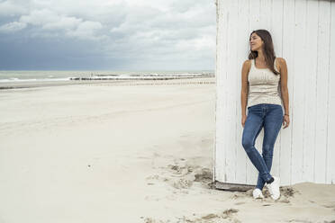 Schöne Frau träumt, während sie sich an eine Strandhütte lehnt - UUF22699