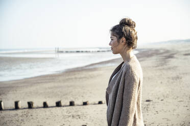 Junge Frau, die am Strand in der Sonne steht und nachdenkt - UUF22701