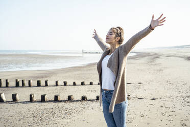 Carefree woman with arms outstretched standing on sand at beach - UUF22703