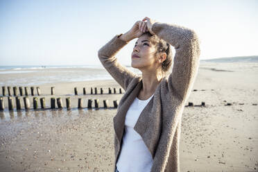 Thoughtful woman looking up against sky at beach - UUF22705