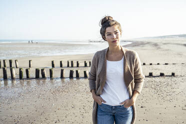 Junge Frau mit Händen in den Hosentaschen schaut weg auf den Strand - UUF22707