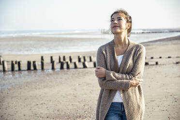 Young woman looking up with arms crossed at beach - UUF22709