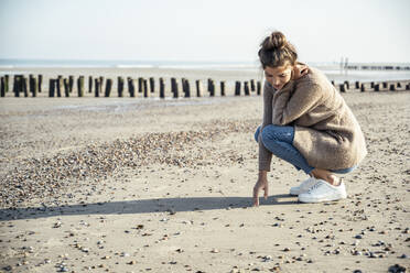 Young woman with squatting position on sand at beach - UUF22710