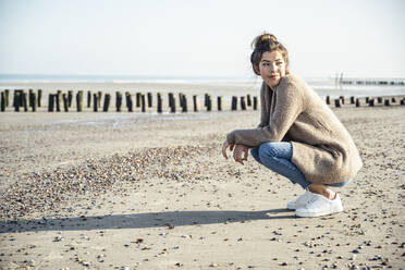 Schöne Frau in der Hocke mit Blick auf den Strand an einem sonnigen Tag - UUF22711