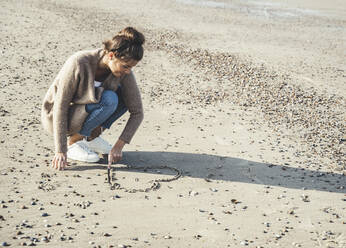 Junge Frau zeichnet Herz auf Sand am Strand - UUF22712