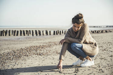 Beautiful woman drawing heart on sand against sky at beach - UUF22713