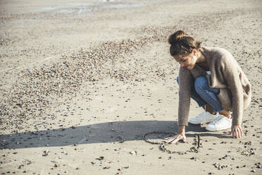Junge Frau hält Hand zwischen Herz auf Sand am Strand gezeichnet - UUF22714
