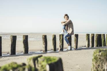 Junge Frau, die am Wochenende auf einem Holzpfosten am Strand sitzt und träumt - UUF22715