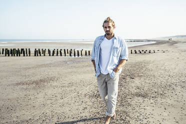 Junger Mann, der an einem sonnigen Tag am Strand spazieren geht - UUF22722