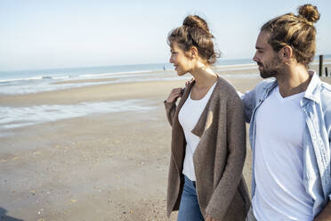 Freund schaut seine Freundin an, während er am Wochenende am Strand spazieren geht - UUF22723