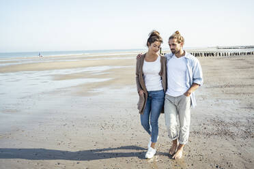 Young couple with hands in pockets taking walk on beach during sunny day - UUF22726